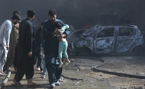 Seorang pria menggendong seorang anak berjalan menjauhi mobil-mobil yang terbakar akibat  ledakan bom, di Quetta, Pakistan, Minggu (24/05/2026). 6).