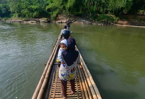 Warga dengan kendaraan motornya menggunakan rakit bambu untuk menyeberangi Sungai Cisadane di kawasan Ciseeng, Bogor, Jawa Barat, Kamis (11/06/2026).