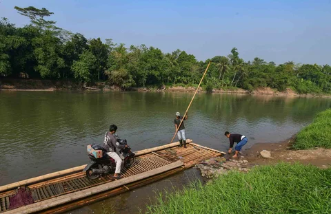 Warga dengan kendaraan motornya menggunakan rakit bambu untuk menyeberangi Sungai Cisadane di kawasan Ciseeng, Bogor, Jawa Barat, Kamis (11/06/2026).
