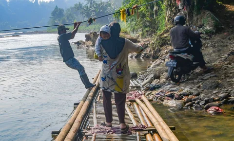 Warga dengan kendaraan motornya menggunakan rakit bambu untuk menyeberangi Sungai Cisadane di kawasan Ciseeng, Bogor, Jawa Barat, Kamis (11/06/2026).