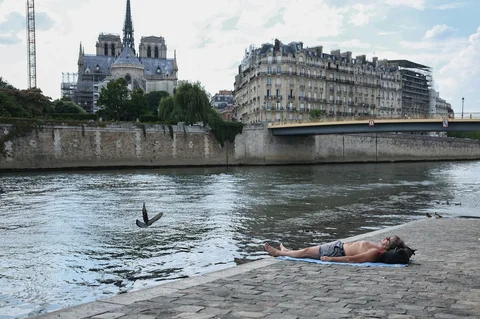 Seorang pria berjemur di Ile Saint-Louis di depan Katedral Notre-Dame di pusat kota Paris, perancis, Kamis. (18/06/2026).