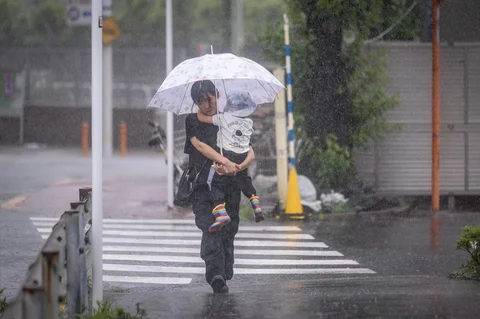 Seorang wanita menggendong anaknya berjalan menerobos hujan deras akibat badai tropis dahsyat Jangmi di Tokyo,  Rabu (03/06/2026).