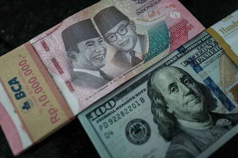 Uang kertas pecahan 100.000 rupiah Indonesia dipajang berdampingan dengan uang kertas pecahan 100 dolar AS di kantor penukaran mata uang di Jakarta,  Kamis (04/06/2026).