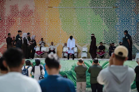Warga menyaksikan saat algojo  mengeksekusi cambuk terhadap terpidana pelanggar hukum syariat Islam perkara bermesraan antara laki-laki dan perempuan yang bukan suami istri (ikhtilath) melalui salah satu media sosial di Taman Bustanussalatin, Banda Aceh, Aceh, Kamis (2/7/2026).