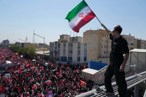 Seorang pria memegang bendera Iran saat truk yang membawa peti jenazah Pemimpin Tertinggi Iran Ayatollah Ali Khamenei dan anggota keluarganya yang terbunuh melintas  di Teheran, Iran, Senin, 6 Juli 2026.