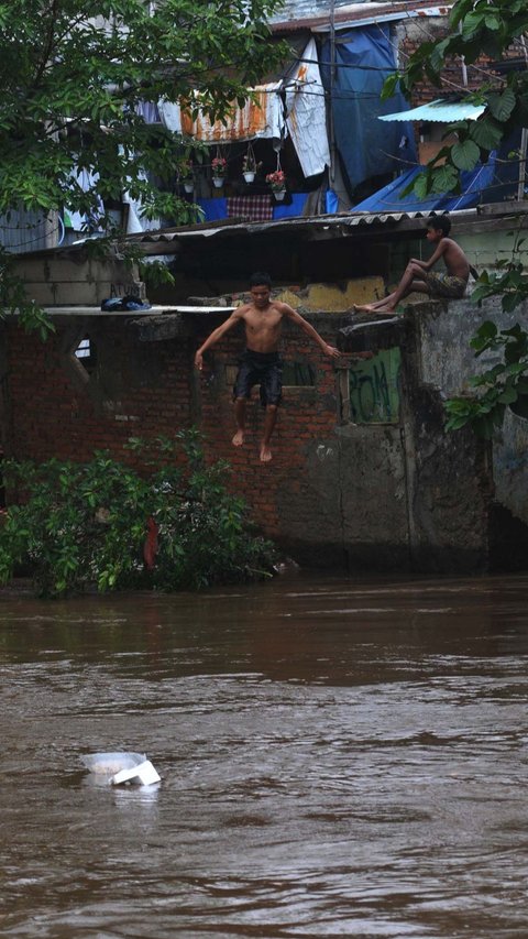 FOTO: Berbahaya! Aksi Nekat Anak-Anak Bermain di Tengah Derasnya Arus Kali Ciliwung