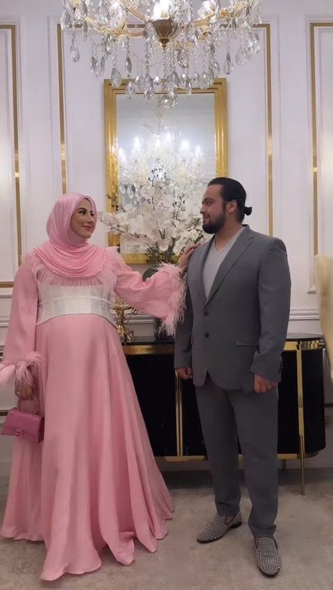 Tasyi yang datang bersama suami nampak serasi. Dimana sang suami mengenakan jas berwarna abu-abu. Sangat cocok dengan dress pinknya.