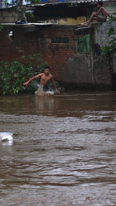 Sejumlah anak melompat pada aliran Kali Ciliwung yang mengalir deras di kawasan Bukit Duri-Manggarai, Jakarta, Selasa (2/7/2024). Merdeka.com/Imam Buhori
