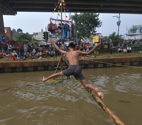 Seorang peserta mencoba melewati bambu yang telah dilumuri oli untuk mencapai pinang dalam lomba Titian Bambu di aliran Kalimalang, Jakarta Timur, Sabtu (24/8/2024). Semangat perayaan HUT ke-79 Kemerdekaan RI masih terasa di lingkungan RW 04 Kelurahan Cipinang Melayu, Makassar, Jakarta Timur. Foto: Merdeka.com/Imam Buhori