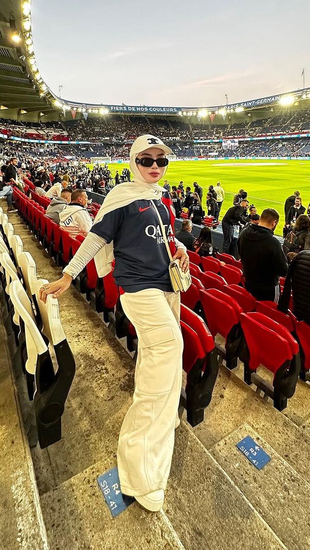 Pose di tribun, Shella pakai kaus jersey dipadukan dengan manset putih