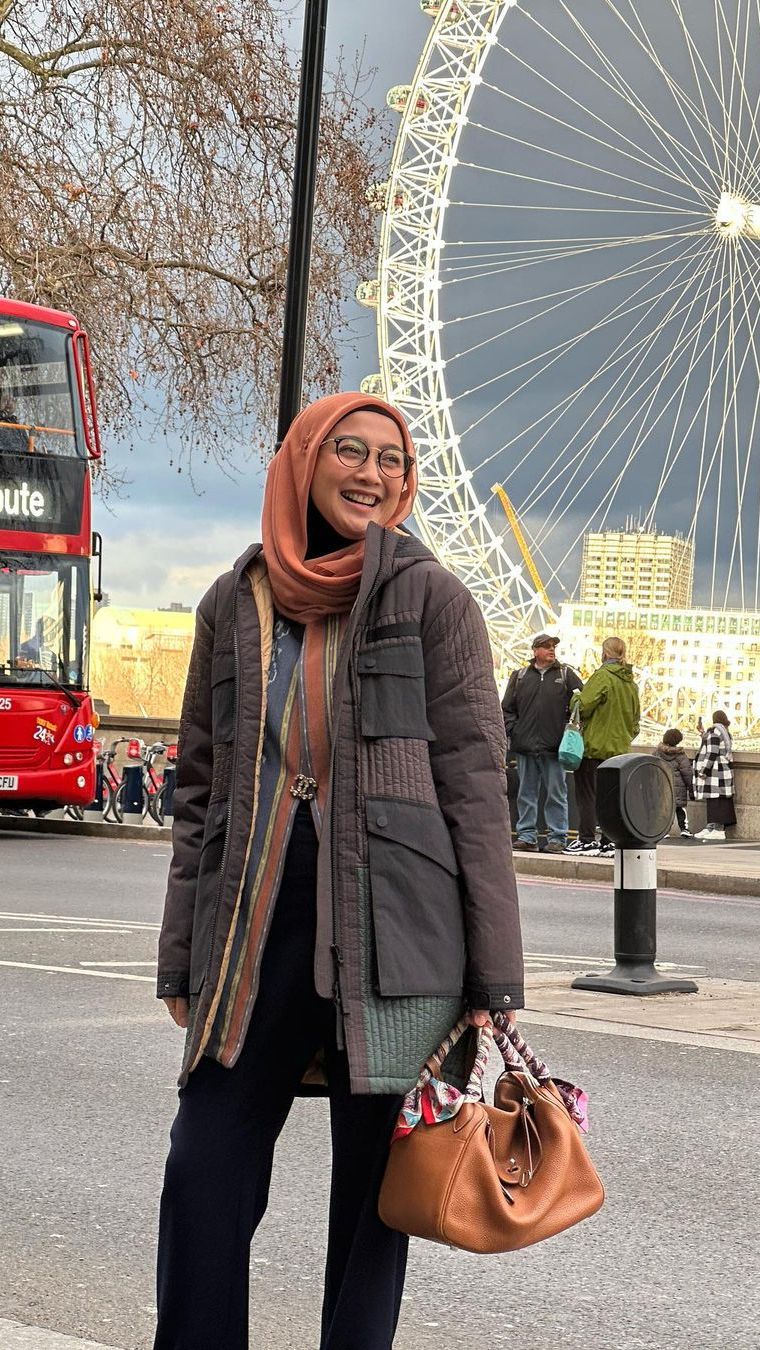 Gaya Desy Ratnasari saat liburan ke luar negeri, tampil santai mengenakan coat dengan riasan sederhana.