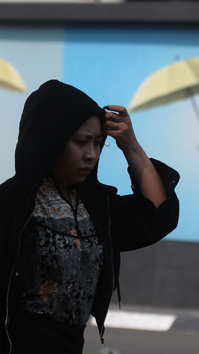Pejalan kaki mengenakan jaket hoodie untuk menghindari panas matahari di kawasan Kuningan, Jakarta, Selasa (26/9/2023).