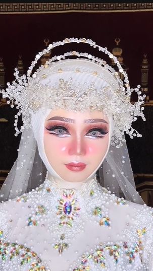 Wajah pengantin terlihat begitu berbeda dengan blush on pink, serta highlighter di bagian pipi. Selain itu area matanya dibentuk ala eye doll sehingga mirip Barbie