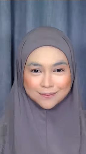 Wajahnya pun mulai ditutupi oleh foundation dan shading. Ia juga masih menggunakan hijab biasa sebelum nantinya di rias ala pengantin Minang