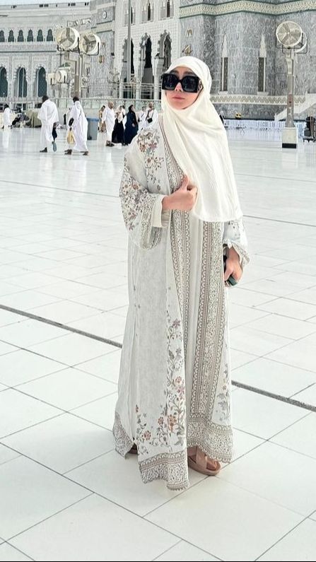 Berpose di masjidil haram, Amy terlihat kece dengan dress putih bermotif dan kaca mata besar.