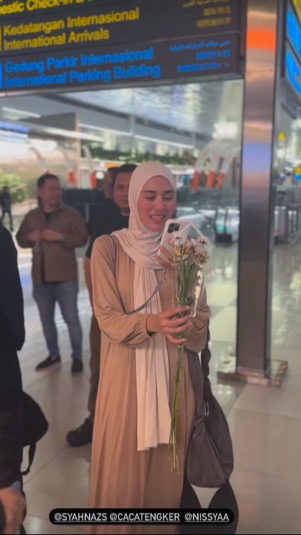 Jeje menyambut istrinya sambil membawakan sebuket bunga sebagai hadiah.