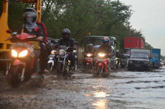 Sejumlah pengendara sepeda motor melewati genangan air di ruas Jalan C 