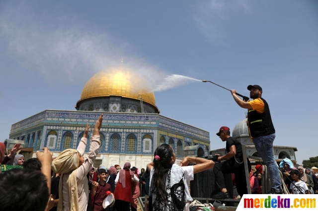 Seorang pemuda Palestina menyemprotkan air pada anak-anak untuk mendinginkan mereka sebelum melaksanakan salat pada hari Jumat terakhir bulan suci Ramadan di dekat Kubah Batu, Yerusalem (31/5).