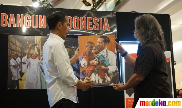 Presiden Joko Widodo atau Jokowi melihat salah satu foto saat mengunjungi pameran 'Membangun Indonesia' di Mall Neo Soho, Jakarta Barat, Selasa (12/11). Jokowi mengaku terkesima dengan foto dirinya yang sedang menggendong anak Papua.
