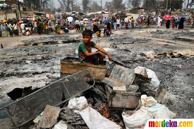 Seorang anak etnis Rohingya duduk di atas tumpukan barang-barang yang hangus terbakar di sebuah kamp pengungsian di Cox's Bazar, Bangladesh, pada 24 Maret 2021. Setidaknya 15 orang tewas dalam kebakaran dahsyat yang melanda kamp pengungsi Rohingya di Bangladesh, sementara setidaknya 400 orang masih hilang, kata Badan Pengungsi PBB pada Selasa (23/3/2021).