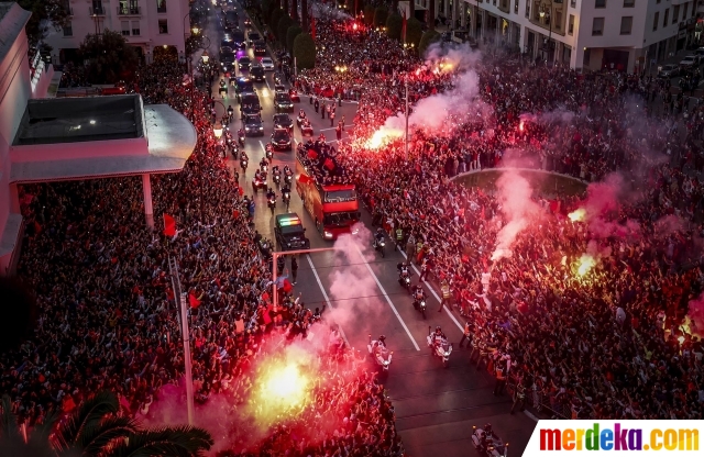 Suporter menyalakan suar dan bersorak saat timnas Maroko tiba di pusat Ibu Kota Rabat, Maroko, pada 20 Desember 2022. Meski pulang tanpa trofi Piala Dunia 2022, timnas Maroko tetap mendapat sambutan meriah dari suporternya. 