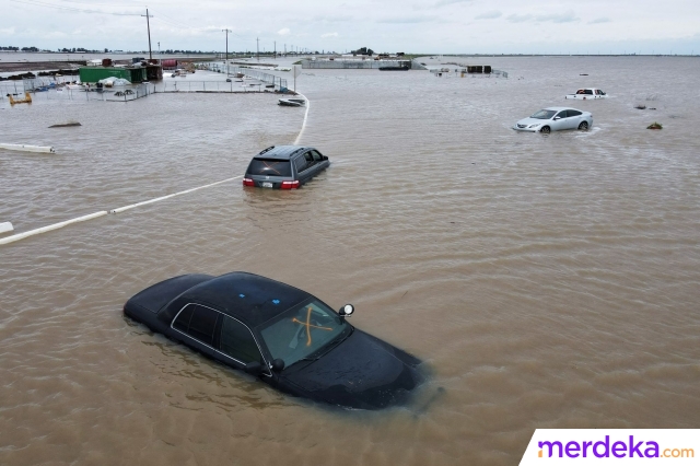 Mobil-mobil terbengkalai terlihat dengan kondisi rusak terendam banjir di sebuah jalan saat luapan air dari Sungai Tule menggenangi area tersebut.