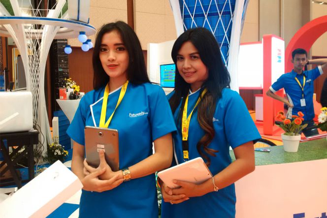 Duet gadis berbaju biru membawa tablet di tangannya yang menampilkan berbagai layanan yang disediakan perusahaan bernama Futuready.