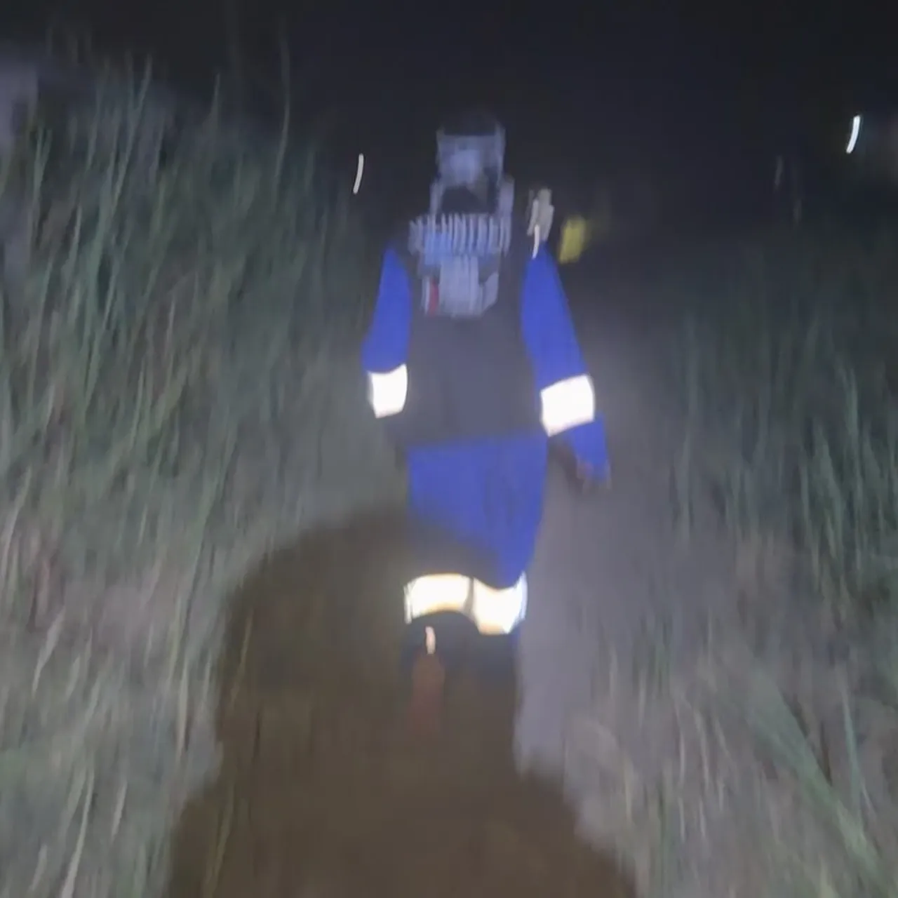 夜の草地を歩く消火活動の関係者。反射材付きの作業着を着ている