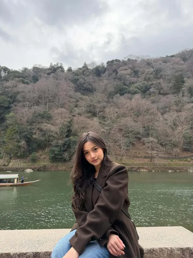 Megan Domani duduk santai dengan latar belakang sebuah sungai.