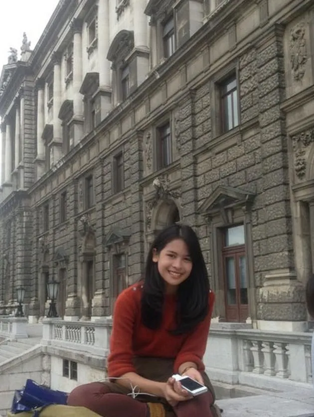 Maudy Ayunda in action memakai sweater rajut warna merah.